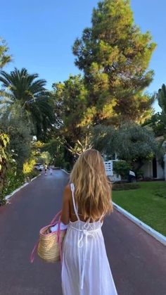 a woman walking down the street with a basket in her hand and palm trees behind her