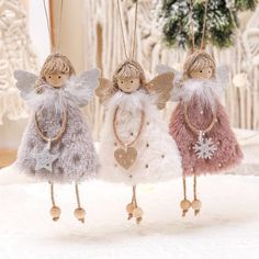 three little angel ornaments hanging from strings on a white surface with snowflakes in the background