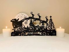 two candles are lit in front of a black and white paper cut out of santa's sleigh