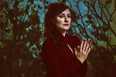 a woman standing in front of a tree with her hands folded up and looking at the camera