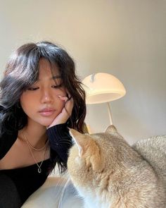 a woman sitting on a couch petting a cat with her hand near her face