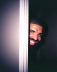 a man with a moustache is peeking out from behind a door and smiling