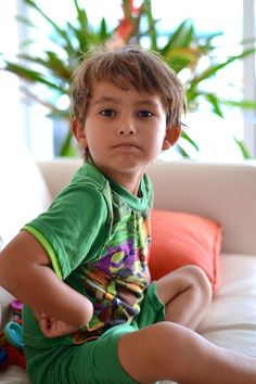 a young boy sitting on top of a white couch next to a potted plant