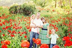 a family standing in a field full of red flowers with their arms around each other