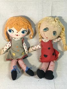 two dolls sitting next to each other on a white surface with one holding the hand of another doll