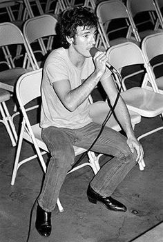 black and white photograph of a man sitting in a chair holding a microphone to his mouth