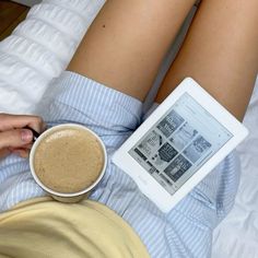 a person laying in bed with a cup of coffee and an ipad