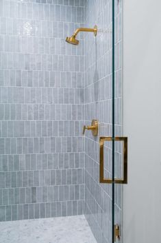 a walk in shower sitting next to a white tiled wall with gold fixtures on it