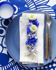 a blue plate topped with flowers next to a fork and knife on top of a table