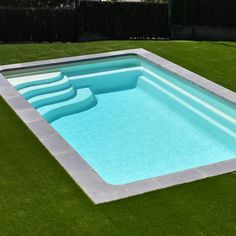 an empty swimming pool in the middle of a lawn area with artificial grass around it