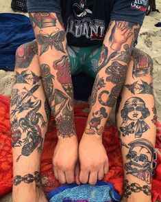 a man sitting on the beach with tattoos on his legs