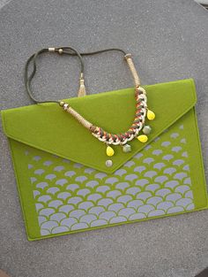 a green purse sitting on top of a cement floor next to a string and beaded necklace