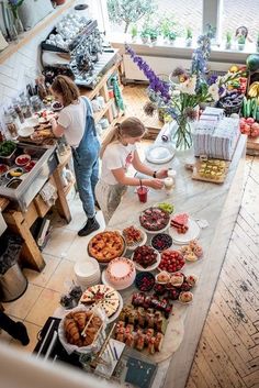 two women preparing food in a kitchen with lots of counter space and flowers on the window sill