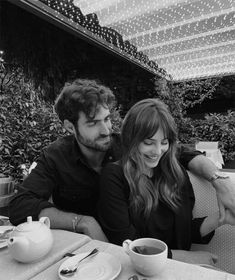 a man and woman sitting at a table with cups of coffee in front of them