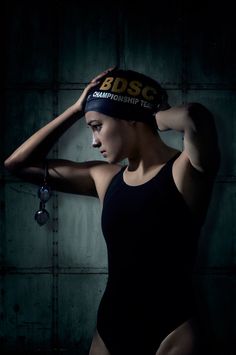 a woman in a black swimsuit is holding her head with both hands and wearing a hat