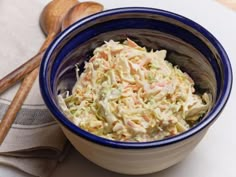 a bowl filled with coleslaw next to two wooden spoons