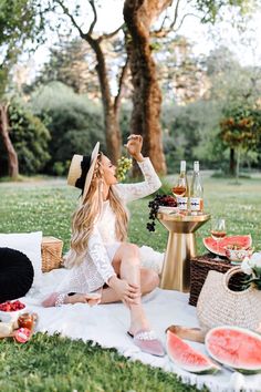 a woman sitting on top of a blanket next to a table filled with watermelon slices