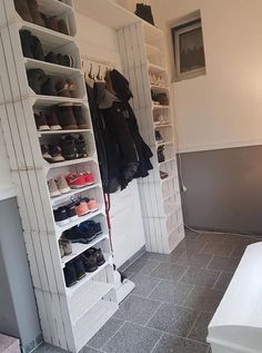 a white closet filled with lots of shoes and clothes hanging on the wall next to a bed