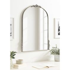 a mirror sitting on top of a white counter next to a vase and potted plant