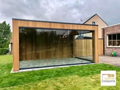 a glass walled room in front of a brick building with grass on the ground and trees behind it