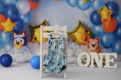 a baby's blue romper is hanging on a chair in front of balloons