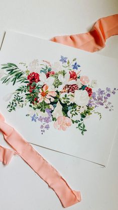 an arrangement of flowers is displayed on top of a piece of white paper with pink ribbon