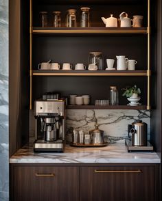 the coffee maker is sitting on top of the marble countertop in front of shelves with cups and mugs