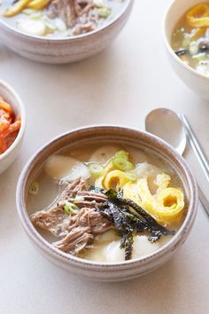 three bowls of soup with meat, vegetables and noodles in them on a white table