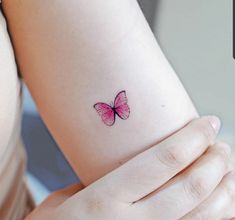 a small pink butterfly tattoo on the wrist