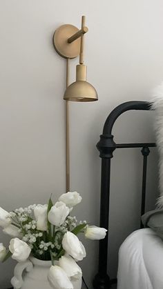 a vase with white flowers sitting on a table next to a lamp and a bed