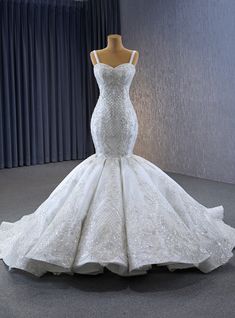 a white wedding dress on display in front of a curtained window with curtains behind it