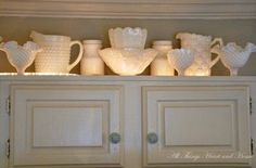 white glass dishes and vases are on top of the cabinet