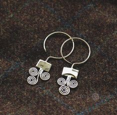 two silver hoop earrings with spiral designs on them sitting on a brown carpeted surface