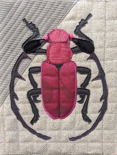 a pink bug with black legs is on a white quilted piece of fabric that has been stitched onto it