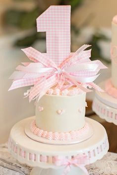 a pink and white cake with the number one on top is sitting on a table