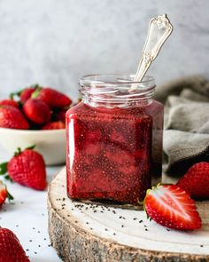 a jar filled with strawberry jam on top of a wooden table next to bowls of strawberries