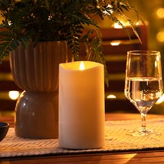 a lit candle sits on a place mat next to a wine glass and potted plant