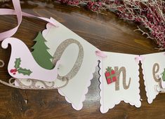 a christmas banner hanging on a wooden table with pink ribbon and decorations around the edges