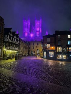 an image of a city at night with purple lighting on the buildings and cobblestone streets