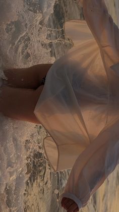 a woman in a white dress standing on the beach with her legs spread wide out