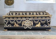 an ornate black and gold casket sitting on top of a stone floor