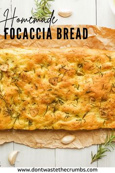 homemade focaccia bread on parchment paper with garlic and rosemary sprigs