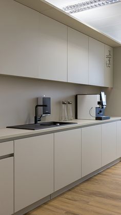 an empty kitchen with white cabinets and counter tops, along with a coffee maker on the wall