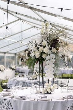 a table set up with white flowers and greenery for a wedding reception in a tent