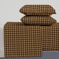 three pillows are stacked on top of each other in front of a bed with brown and white checkered sheets