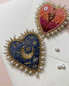 two heart shaped brooches on top of an envelope with pearls and other decorations