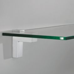 a glass shelf on the wall with a metal hook and two green shelves below it