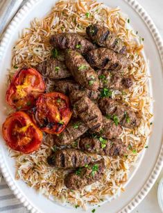 a white plate topped with meatballs and rice next to tomatoes on top of a table