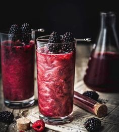 two glasses filled with raspberry and blackberries on top of a wooden table