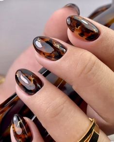 a woman's hand with some brown and black nail polishes on her nails